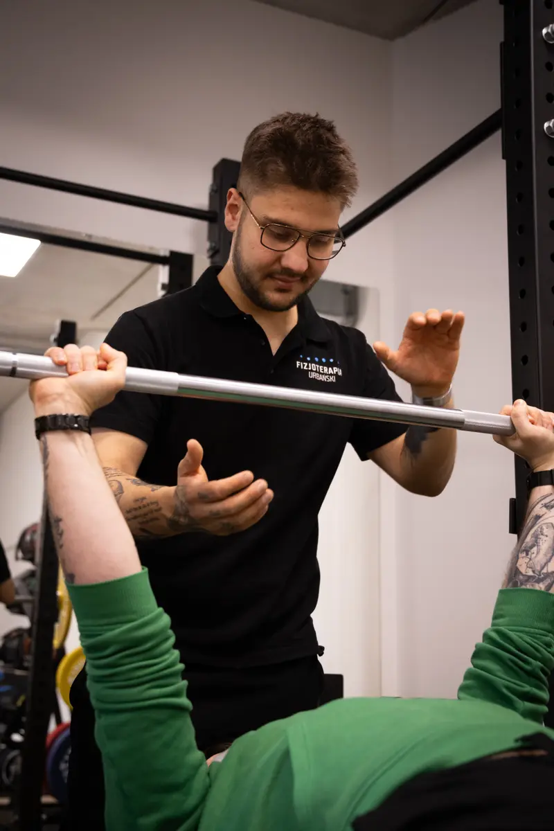 Jakub Gibas asekuruje podopiecznego przy wyciskaniu sztangi